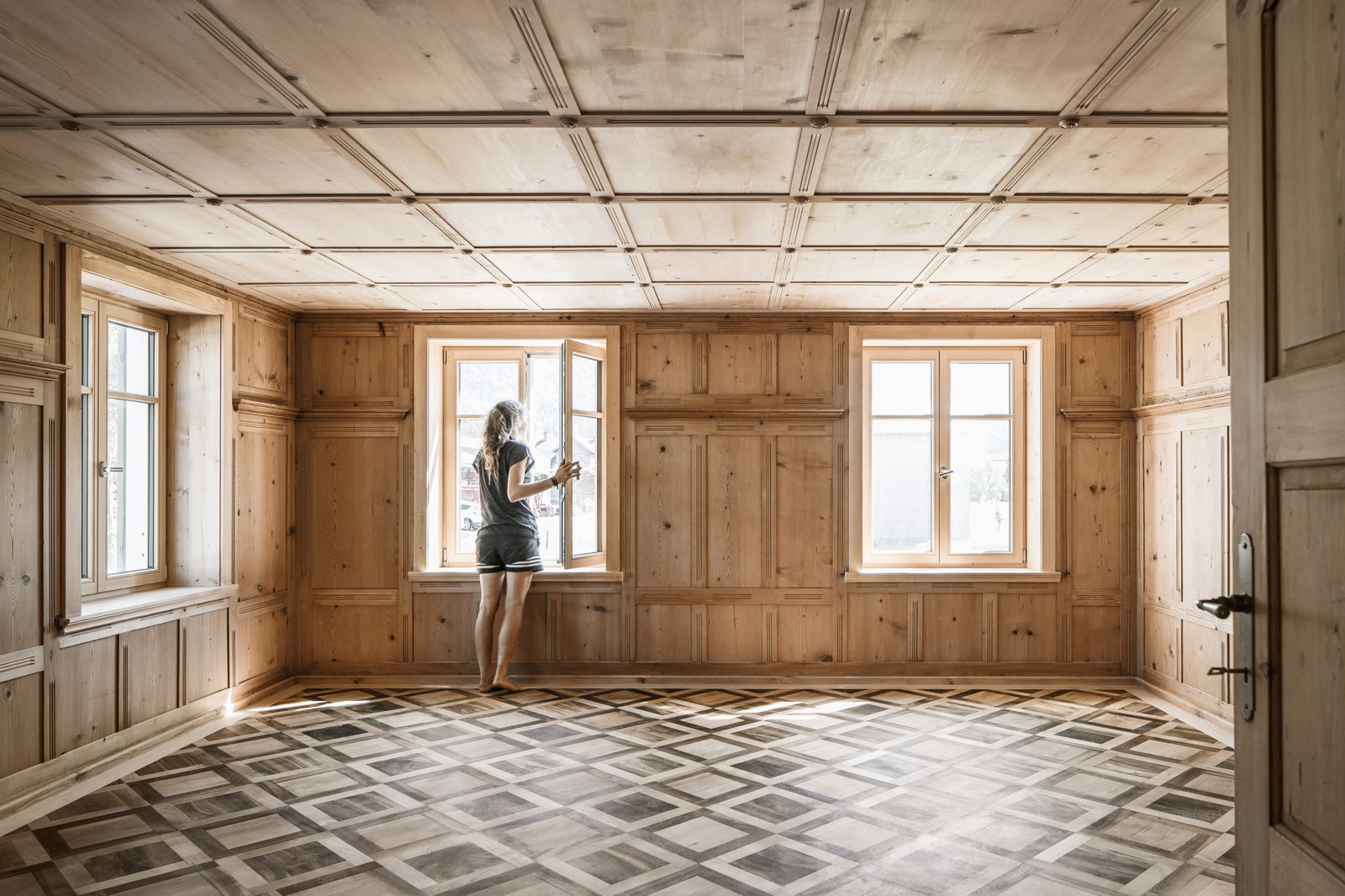 Haus Mitanand Bezau nach der Sanierung. Blick in einen Innenraum mit sanierten Parkettboden, Wand und Decken Kassetten. Bildachweis: Albrecht Schnabel