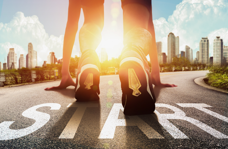 Läuferin in Startposition auf einer Straße mit Aufschrift "START" vor Skyline
